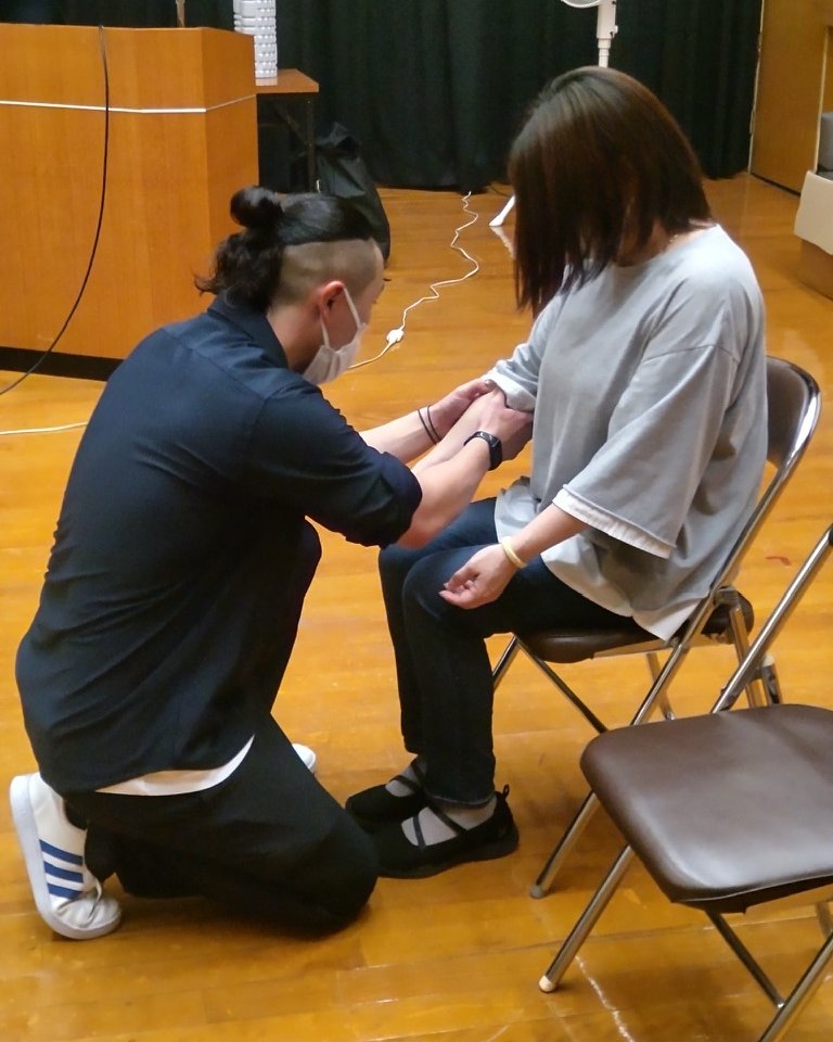 椅子に座った方の前にひざをつき、腕に触れて体を確かめる村田